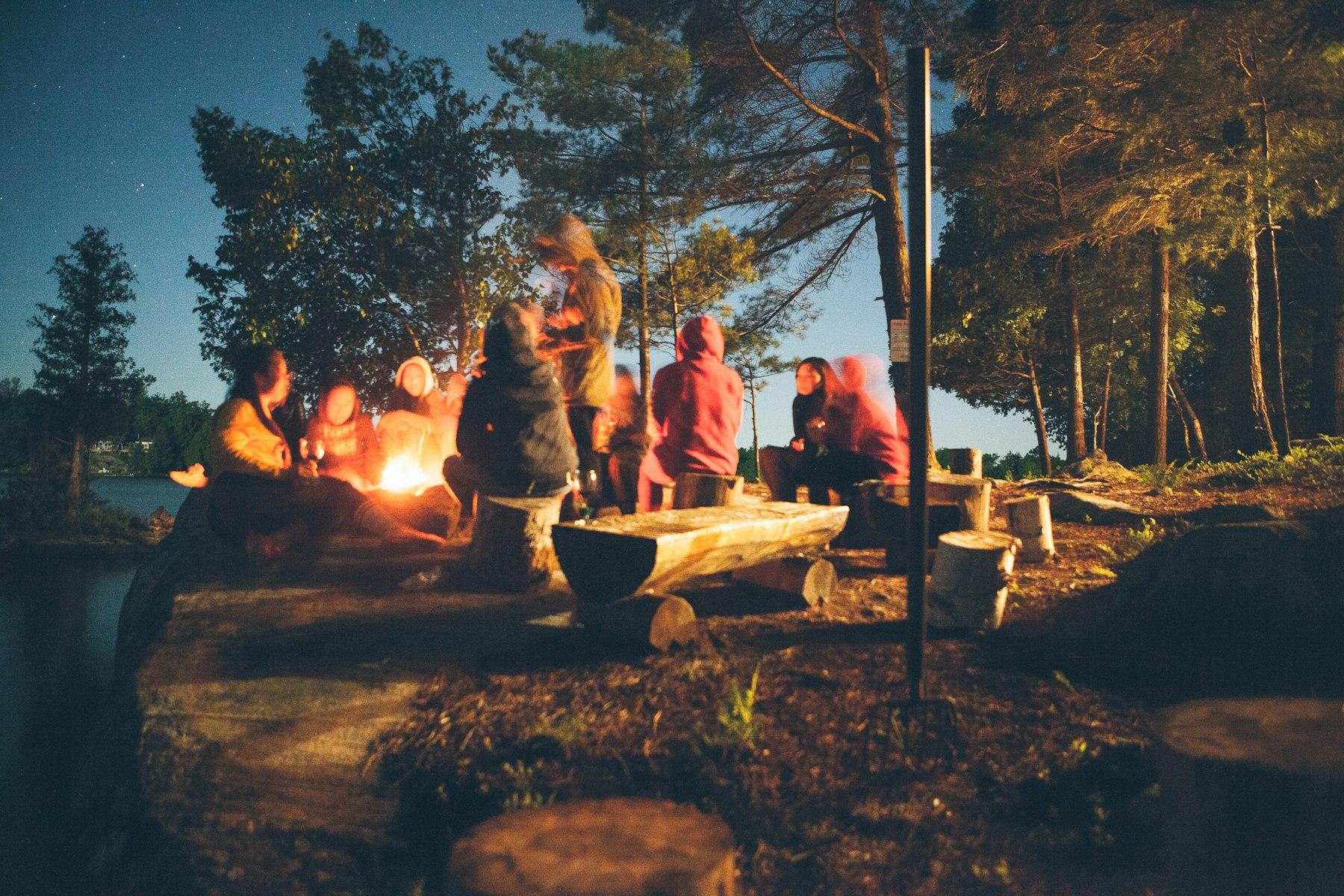 People around a fire beside a lake at night. Stand-in photo.